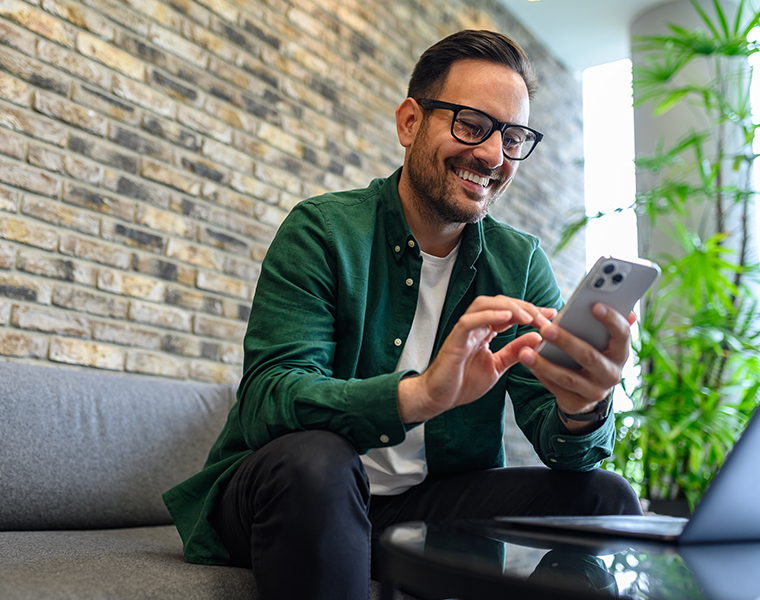 Low angle view of handsome manager checking social media apps over mobile phone on sofa in office