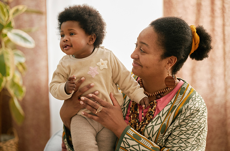 Smiling Black woman wearing colorful patterned clothes holding baby