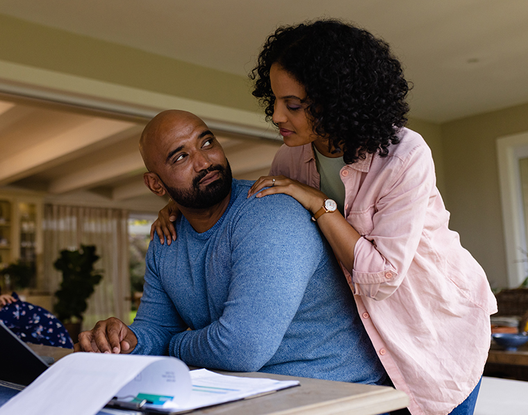 Happy biracial parents using laptop, looking at bills, with daughter in background