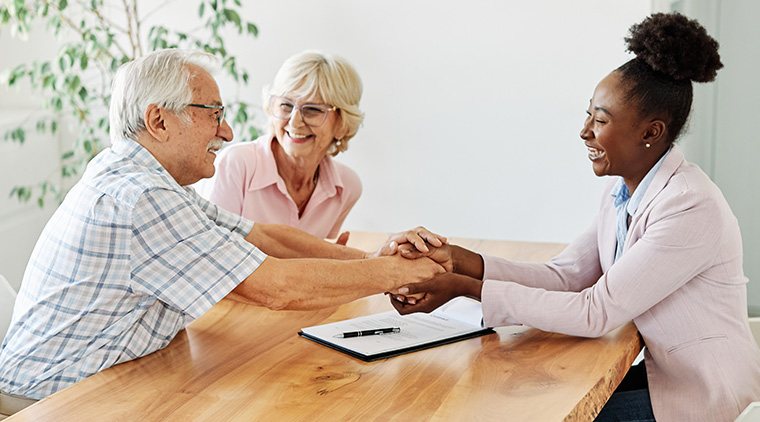 businesswoman shaking hands with senior couple in her office or at their home